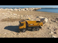 
              1573 dump truck at the beach moving a large rock in its load
            